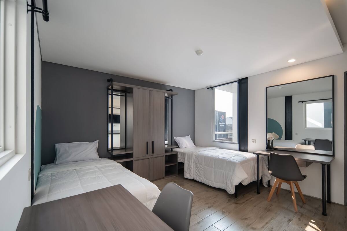 Una habitación de hotel moderna con dos camas, un escritorio, una silla y un espejo grande.