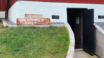 A building with a white exterior and a red door. There is a wooden sign in front of the building that reads 'GARDENBRIEFT WAKOMMEN SPPET'.