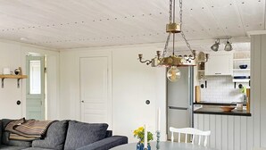 Un salon moderne avec un canapé gris, une table basse ronde surmontée d’un vase, et un coin cuisine doté de meubles blancs et d’un réfrigérateur en acier inoxydable.