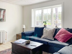 A living room with a blue sofa, a wooden coffee table, a radiator, and a window with curtains. - 4 Star Holiday Home in Mellosa (Flen)