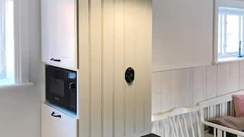 Une pièce avec un meuble blanc, un micro-ondes noir et un berceau blanc avec un coussin rose.