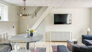 Un salon moderne comprenant un coin repas, un escalier et un téléviseur à écran plat fixé au mur.