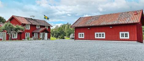 A red wooden building with a flag, a gravel driveway, and a clear sky.