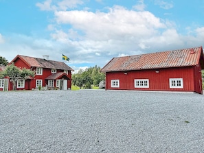 A red wooden building with a flag, a gravel driveway, and a clear sky. - 4 Star Holiday Home in Mellosa (Flen)