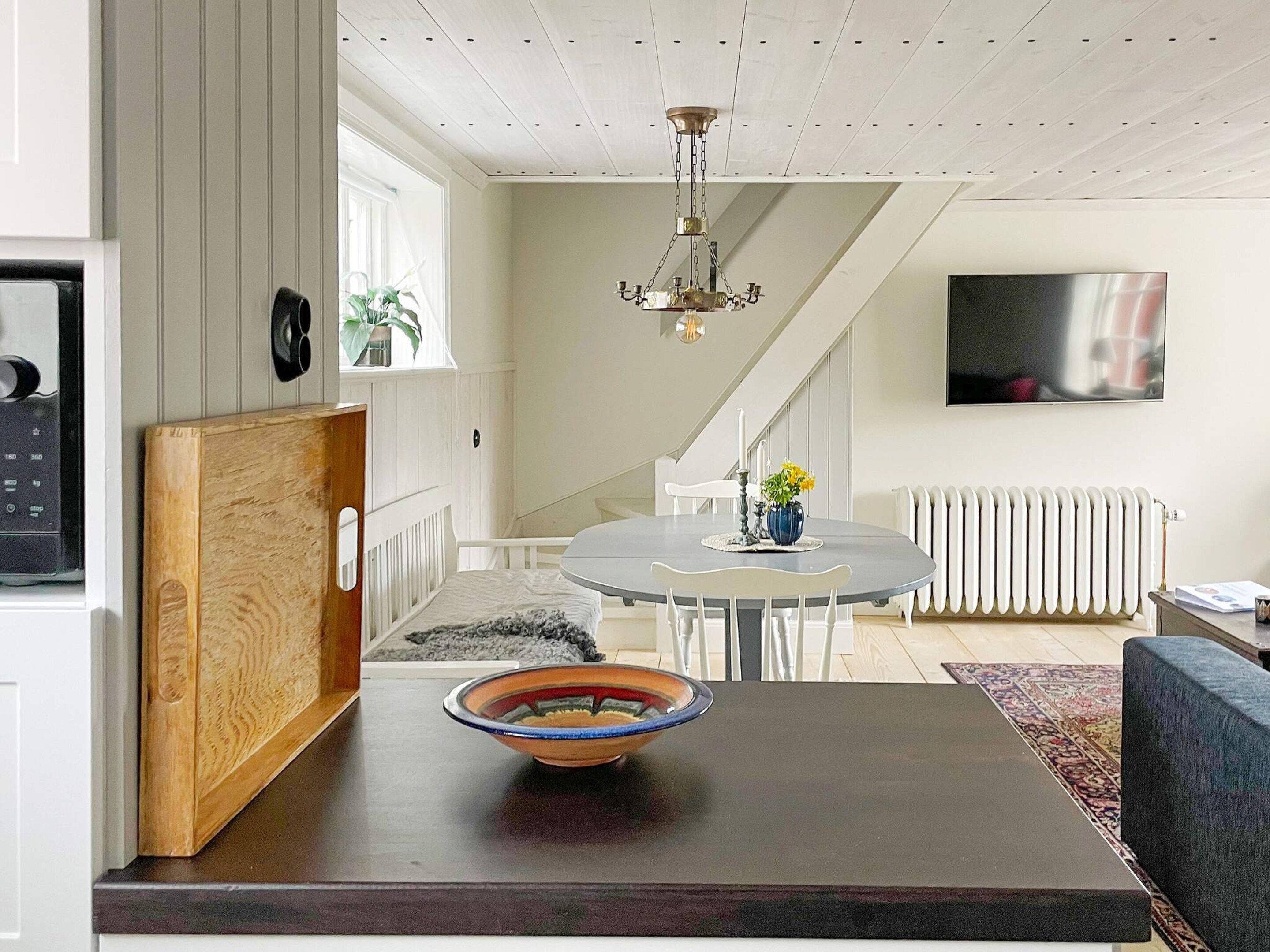 A modern kitchen with a wooden cutting board, a bowl on the counter, and a dining area with a table and chairs.