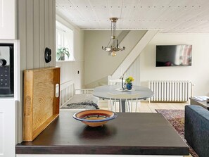 Une cuisine moderne avec une planche à découper en bois, un saladier posé sur le comptoir et un coin repas avec une table et des chaises.