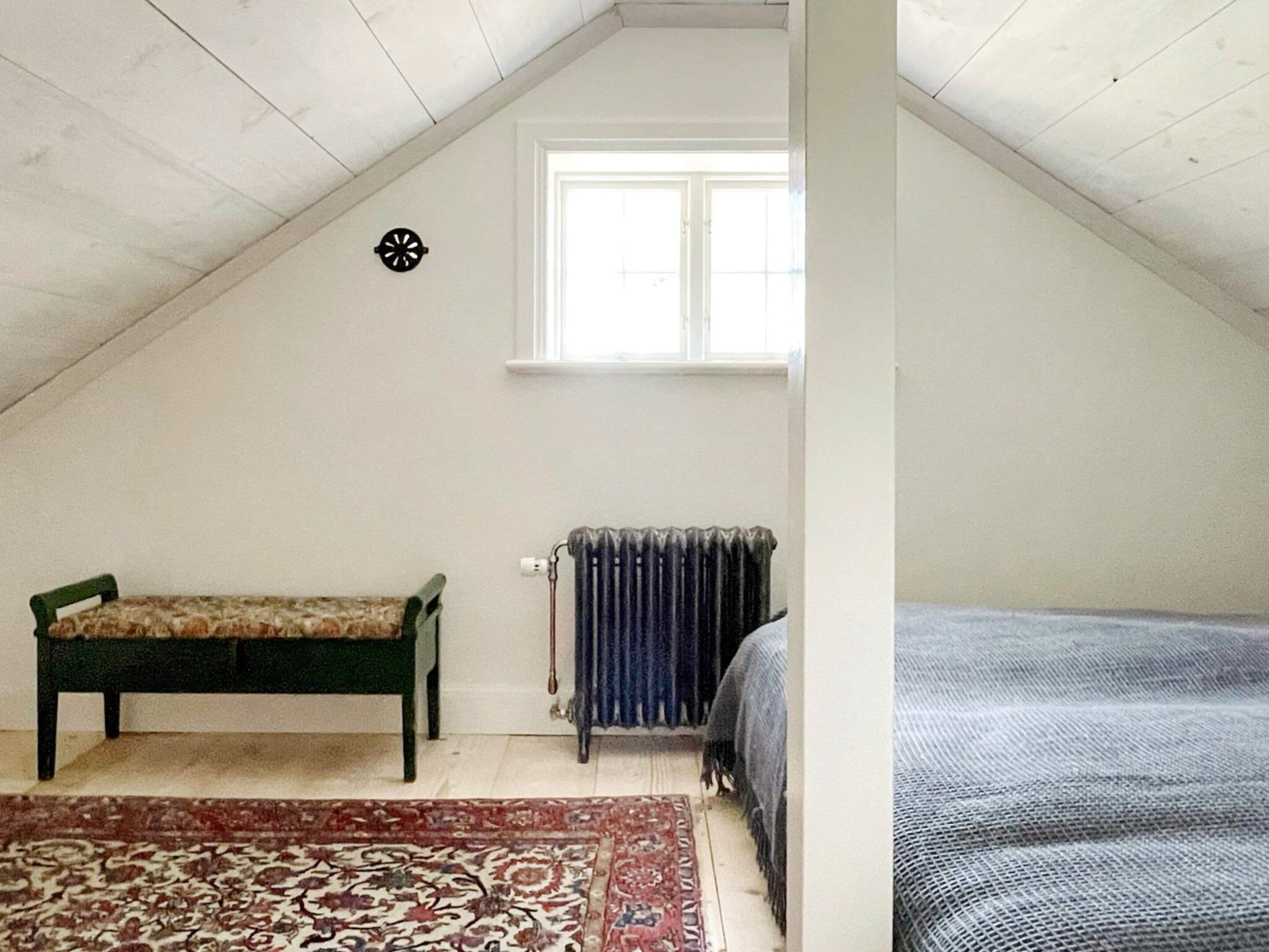 A room with a sloped ceiling, a bench, a radiator, and a bed.