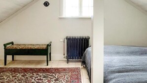 Une pièce avec un plafond en pente, un banc, un radiateur et un lit.