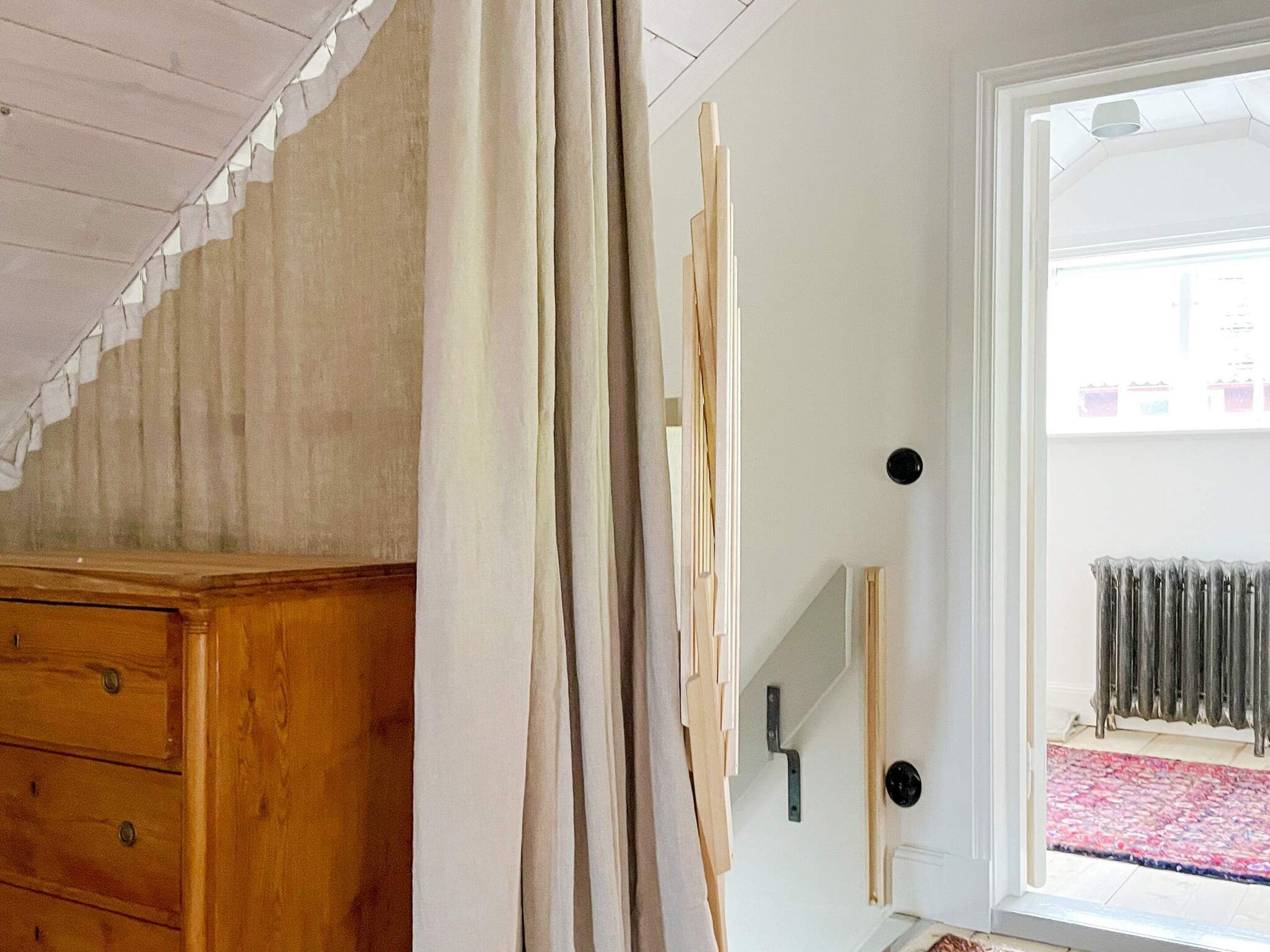 Une pièce avec une commode en bois, une porte dotée d’une poignée noire et, derrière une porte vitrée, on aperçoit un radiateur.