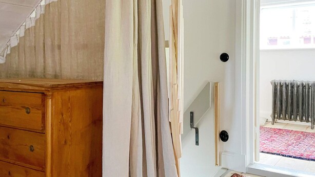 Une pièce avec une commode en bois, une porte dotée d’une poignée noire et, derrière une porte vitrée, on aperçoit un radiateur.