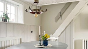 Un coin repas avec une table ronde, des chaises blanches, un lustre, un vase de fleurs et un escalier en arrière-plan.
