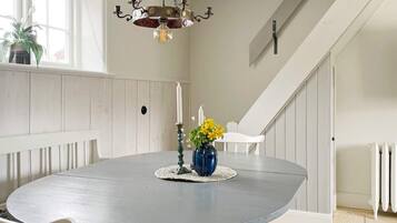 Un coin repas avec une table ronde, des chaises blanches, un lustre, un vase de fleurs et un escalier en arrière-plan.