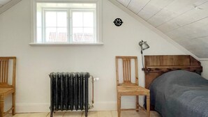 Une pièce avec un plafond en pente, un radiateur, une fenêtre, un lit, une chaise et une lampe.