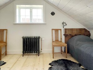 A room with a sloped ceiling, a radiator, a window, a bed, a chair, and a lamp. - 4 Star Holiday Home in Mellosa (Flen)