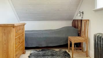 Une petite chambre avec un lit simple, un plafond en pente, une commode en bois, une petite table et un tapis en fourrure sur le sol.