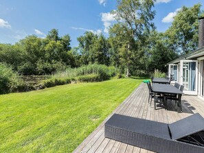 A deck with outdoor furniture, a grassy lawn, and a building with glass doors. - 5 Star Holiday Home in Vejby (Vejby)