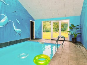 An indoor swimming pool with clear blue walls, a tiled floor, and a view of a green lawn through glass doors. - 5 Star Holiday Home in Vejby (Vejby)