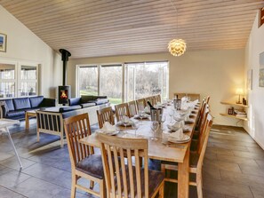 A dining area with a long wooden table set for a meal, a fireplace, and a view of the outdoors. - 5 Star Holiday Home in Vejby (Vejby)