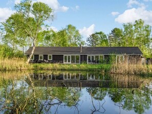 Ein modernes Haus mit einer großen Glasfront, umgeben von einer natürlichen Landschaft und einem Gewässer.