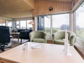 A room with a dining table, two armchairs, a sofa, and a large window offering a view of the outdoors.