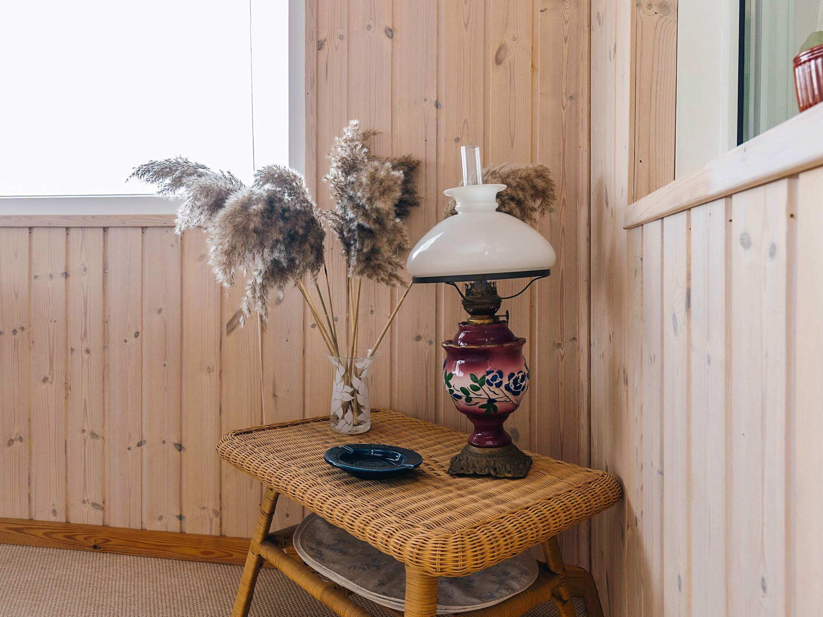 Une table en osier ornée d’un vase contenant des herbes des pampas séchées et d’une lampe décorative.