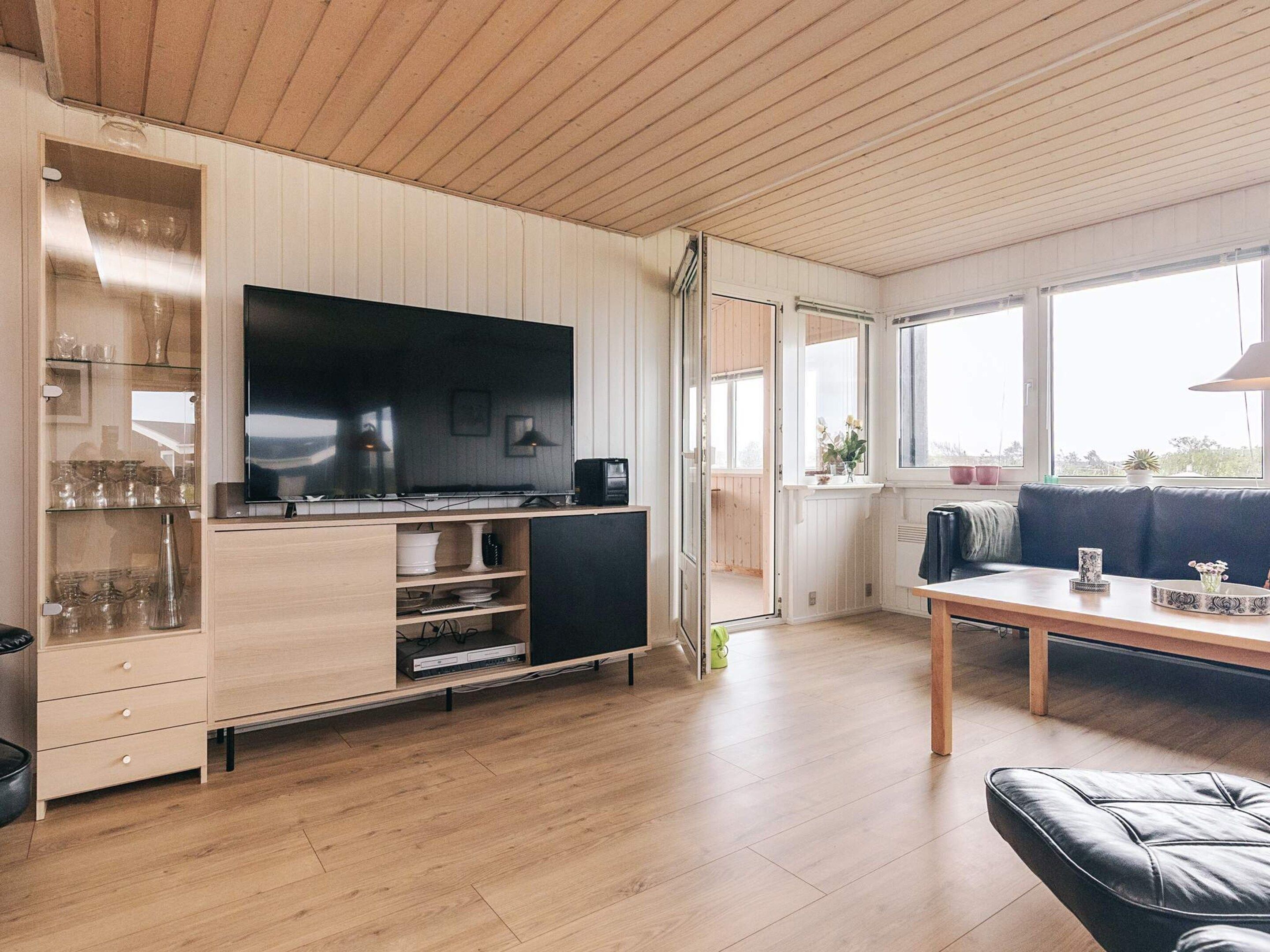 A modern living room with a flat-screen TV, wooden cabinets, a dining table, and a black leather sofa.
