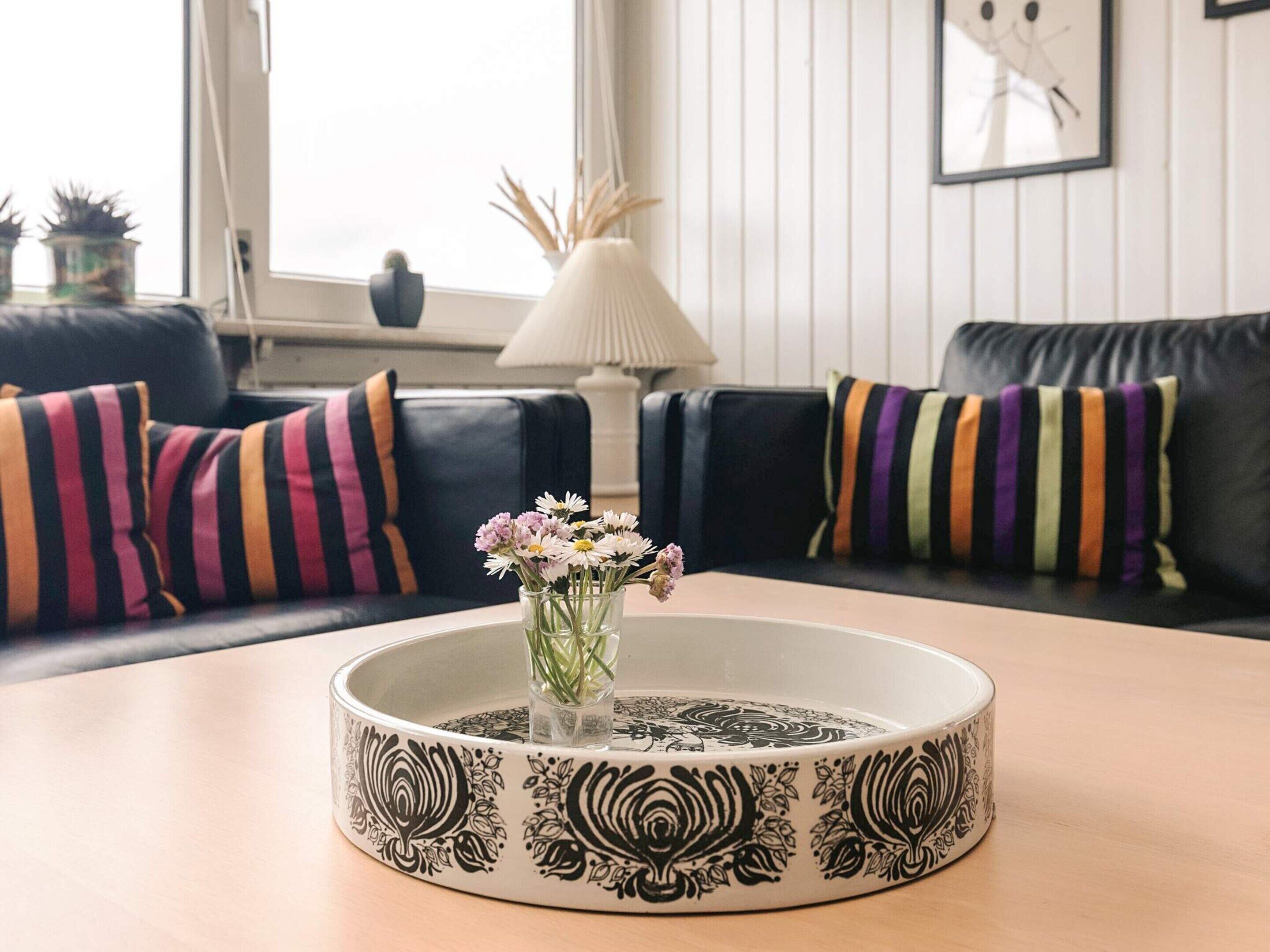 A living room with a round coffee table, black and white patterned tableware, and striped pillows on a black sofa.
