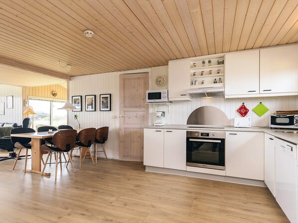 A modern kitchen with white cabinets, a microwave, a stove, and a coffee maker. There is a dining area with a table and chairs.