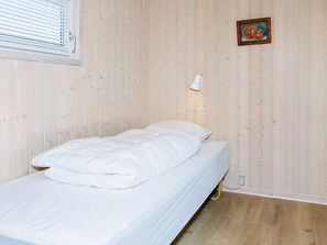 A single bed with a white duvet in a room with wooden panel walls and a small picture frame on the wall.