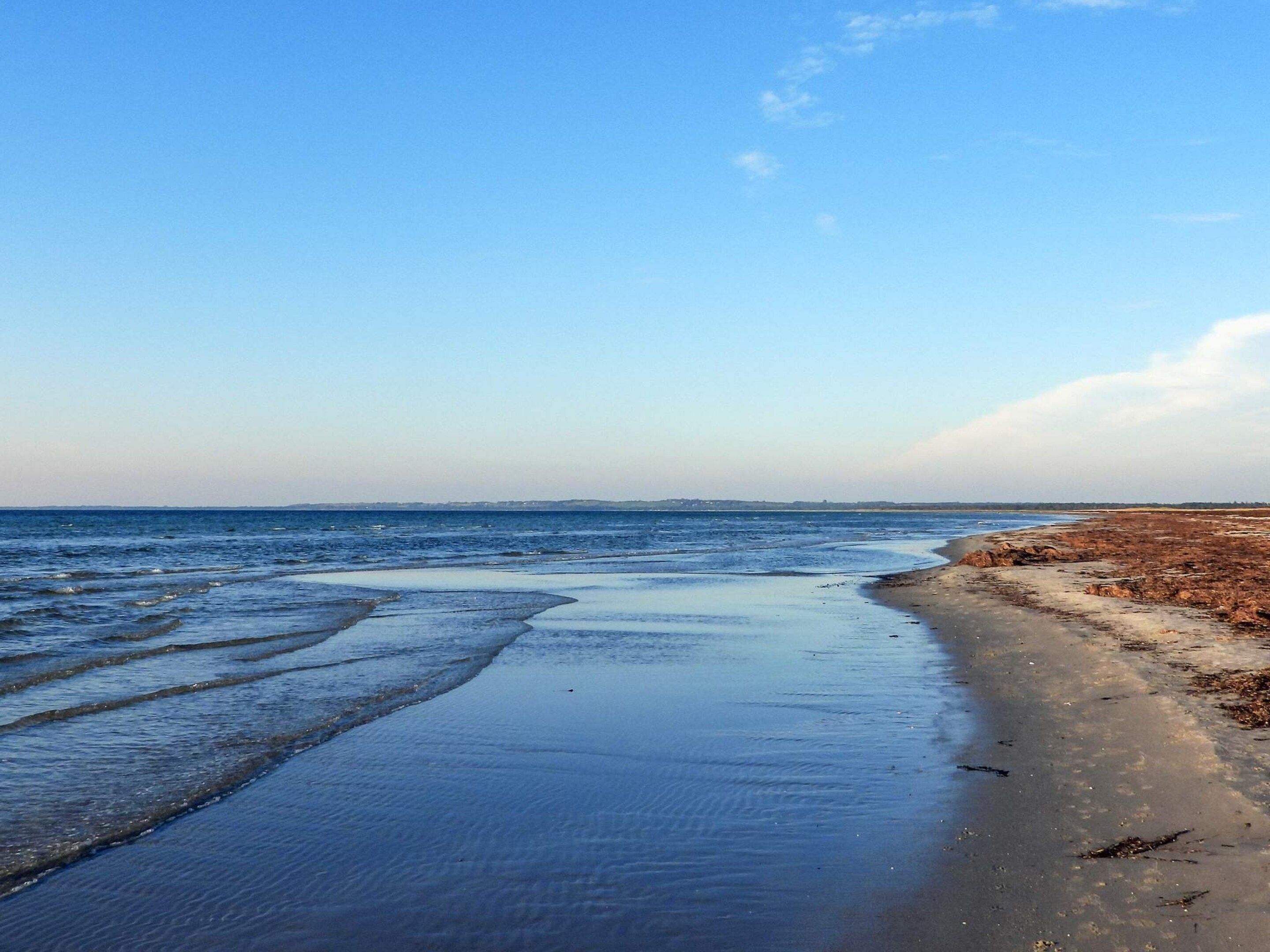 En strand med stilla vatten, en sandstrand och en klar himmel.