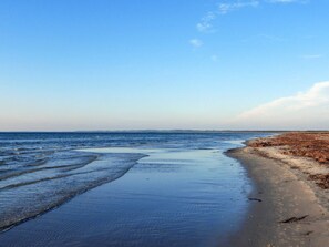 En strand med stilla vatten, en sandstrand och en klar himmel.
