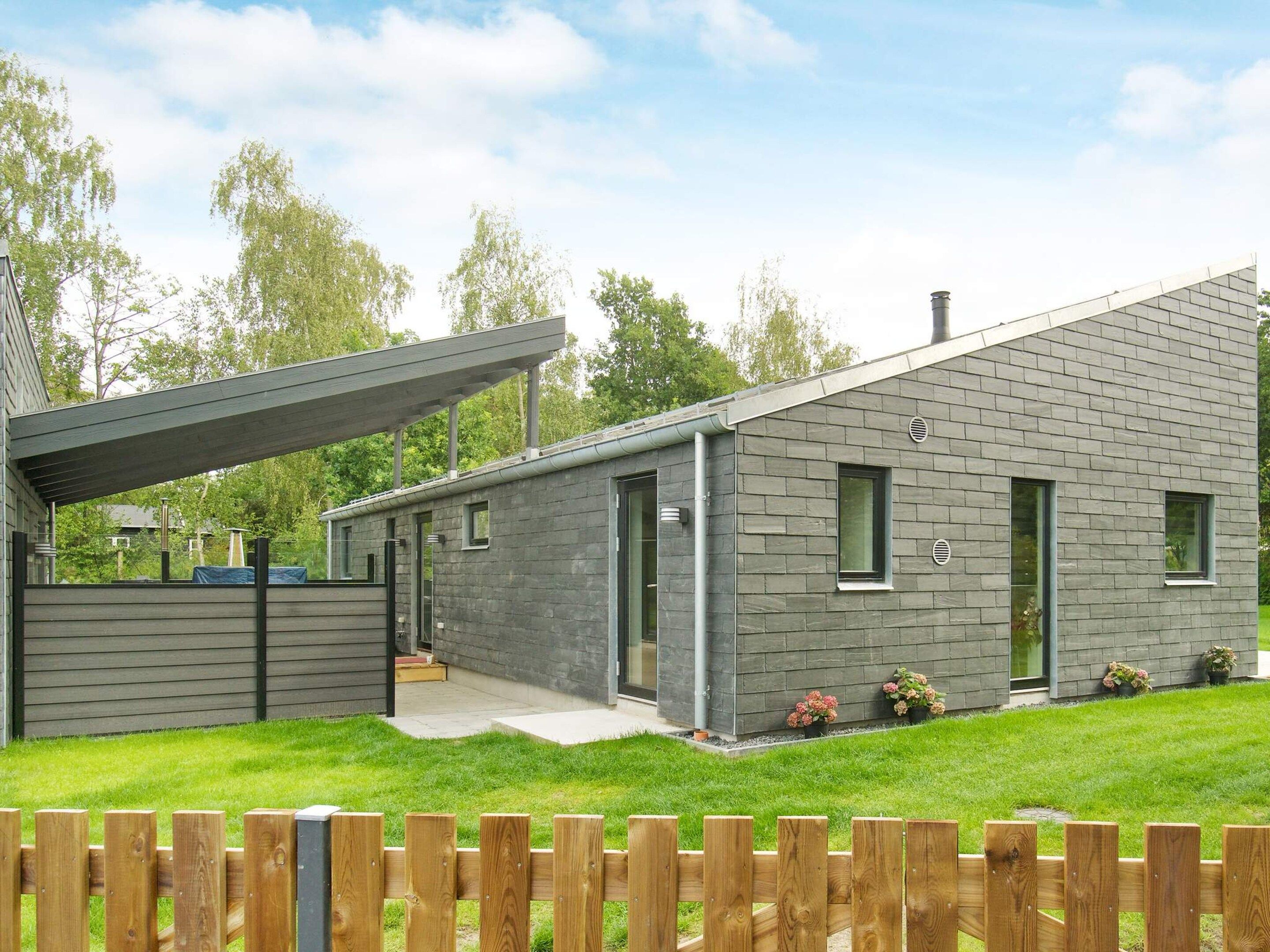 A modern two-story house with a covered porch, a well-maintained lawn, and a wooden fence.