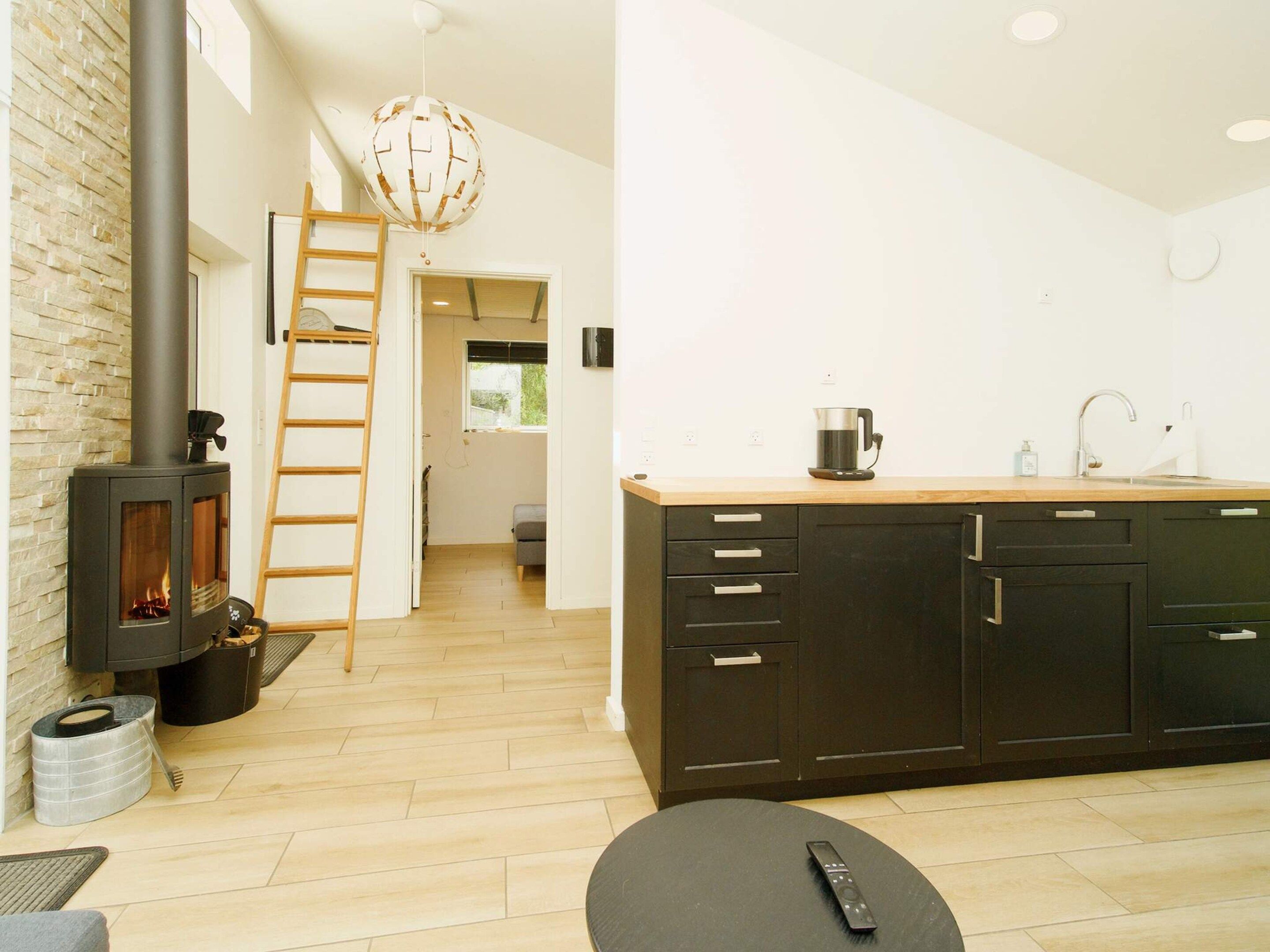 A modern kitchen with a central island, a stove, and a ladder leading to an upper level.