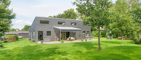 A modern two-story house with a covered patio, surrounded by a well-maintained lawn and trees.