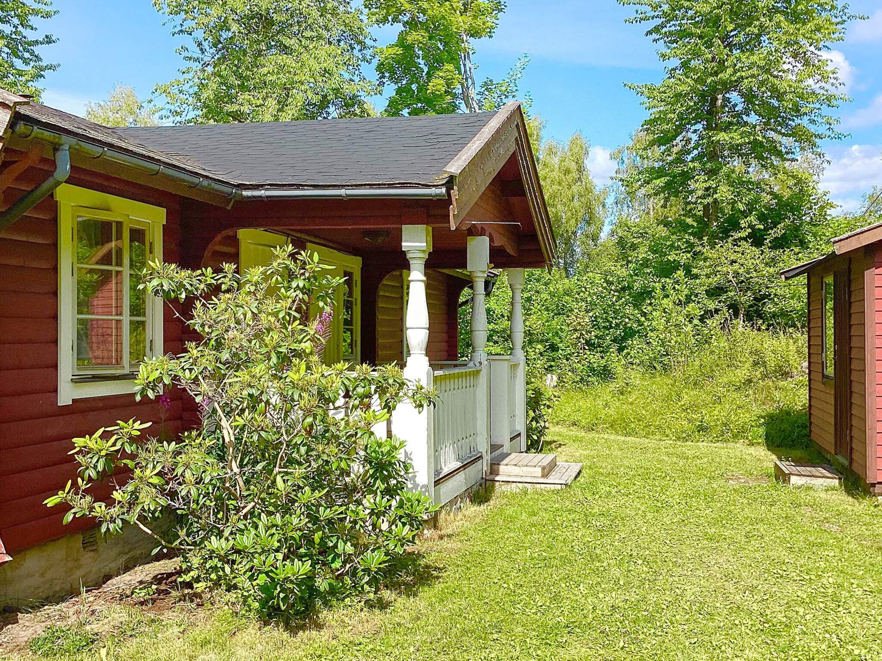 A wooden house with a porch, surrounded by a grassy yard and trees.