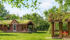 A rustic cabin with a thatched roof, a wooden porch, and a small attached structure with a green roof. - 6 Person Holiday Home in Roslev (Roslev)