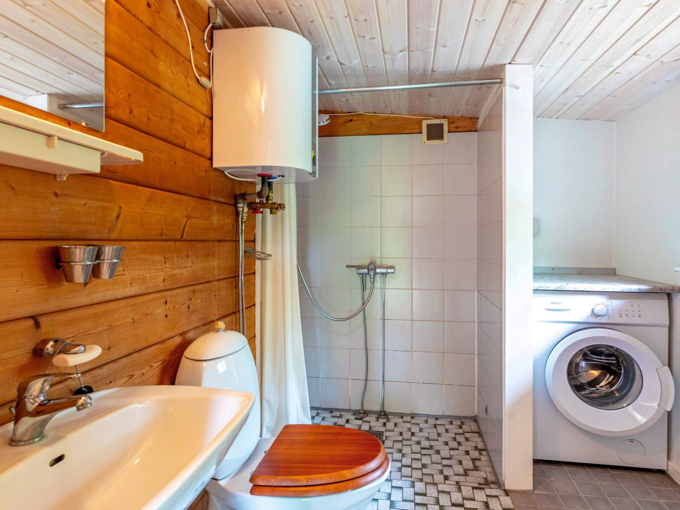 A compact bathroom with a wooden vanity, a toilet, a sink, a shower, and a washing machine.