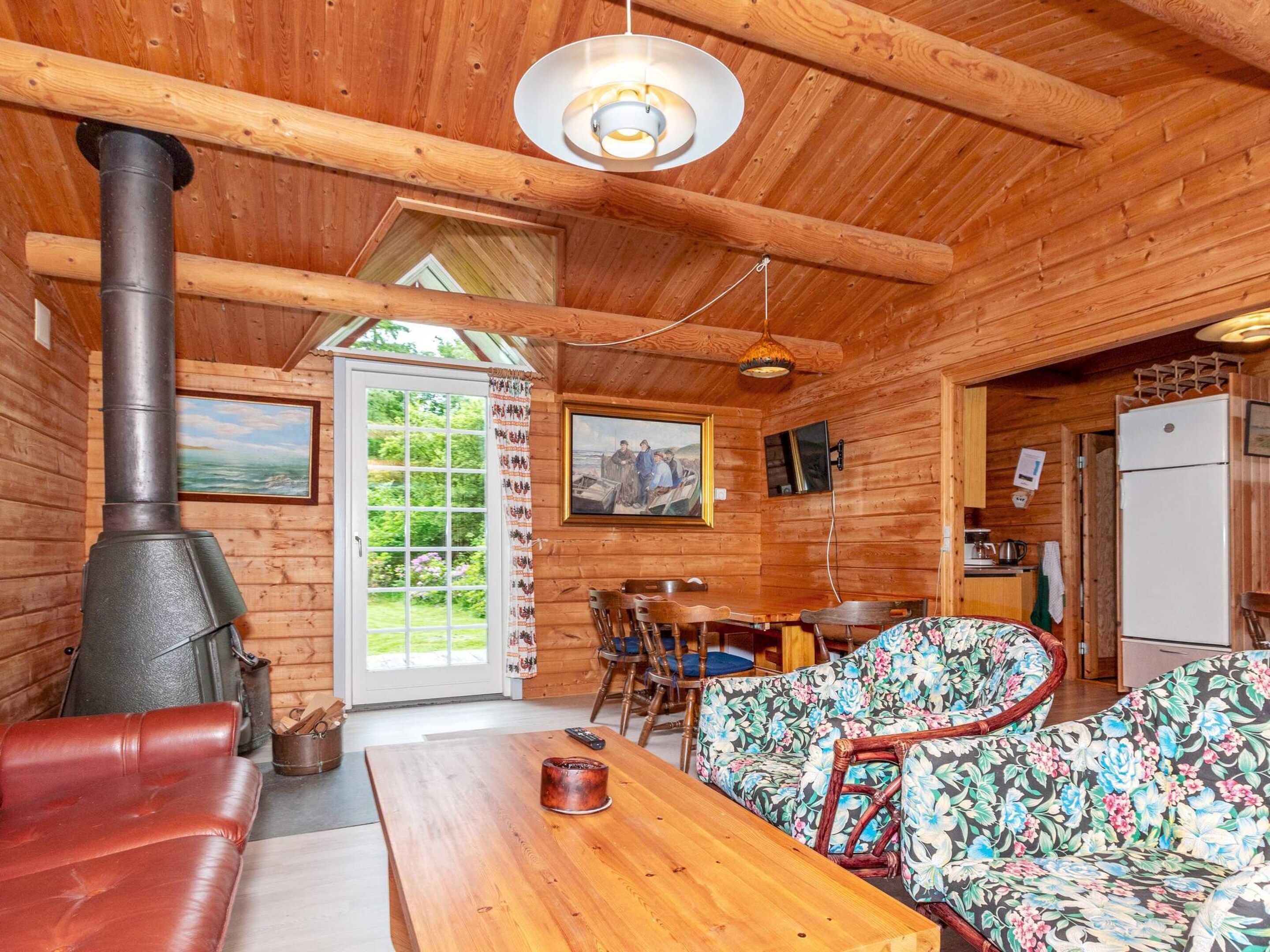 L’intérieur d’un chalet en bois comprend une grande cheminée, un coin repas et un canapé recouvert d’un tissu à motifs floraux.
