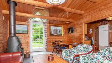L’intérieur d’un chalet en bois comprend une grande cheminée, un coin repas et un canapé recouvert d’un tissu à motifs floraux.