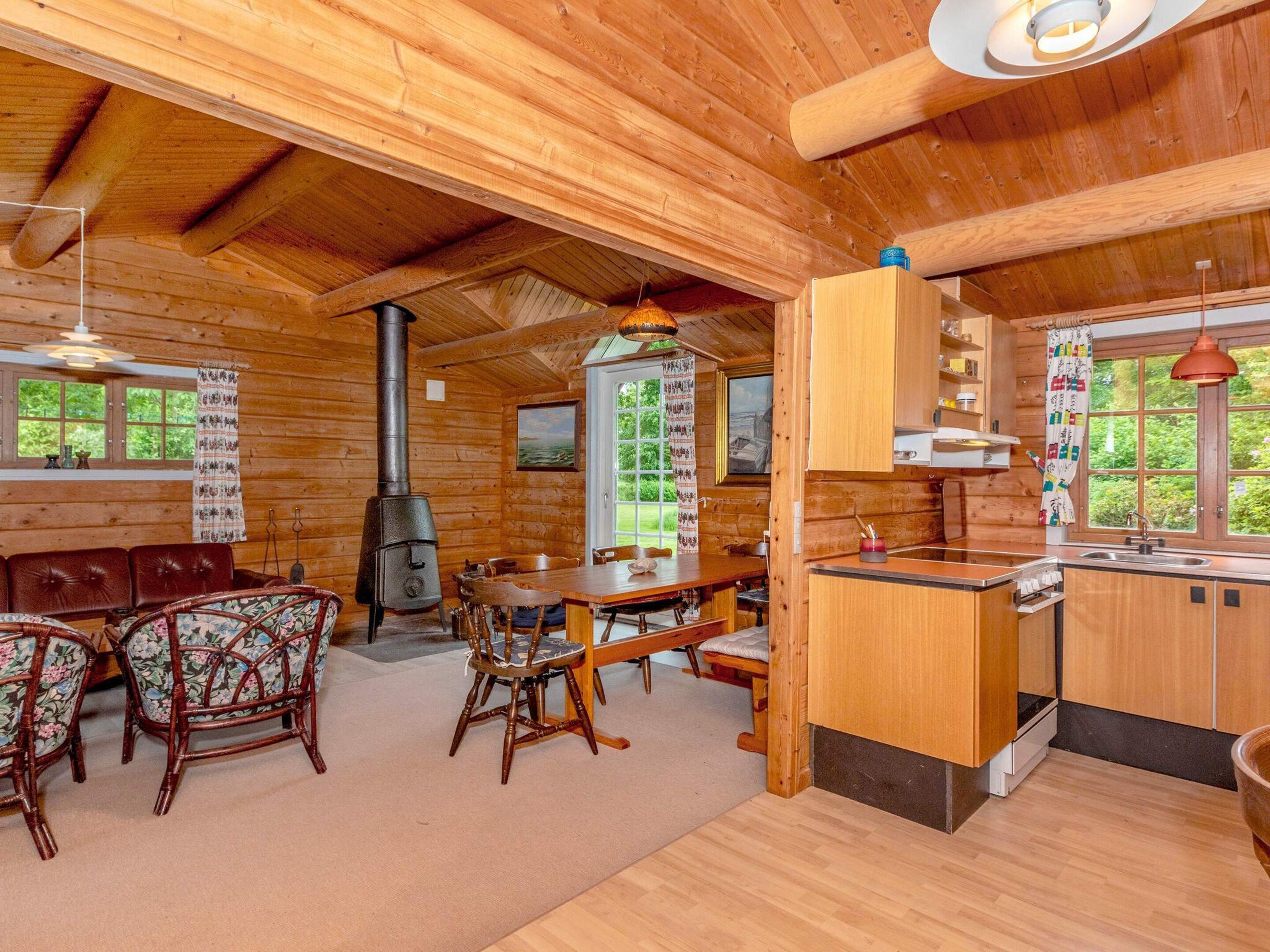 A wooden cabin interior with a dining area, kitchen, and a wood stove.