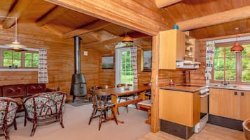 A wooden cabin interior with a dining area, kitchen, and a wood stove.
