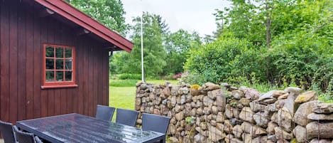 A wooden cabin with a red roof, a stone wall, and a table with chairs outside.