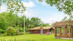 A house with a green roof, a grassy yard, and a garden with yellow flowers. - 6 Person Holiday Home in Roslev (Roslev)