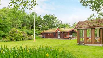 A house with a green roof, a grassy yard, and a garden with yellow flowers.