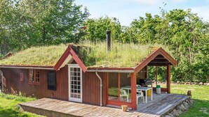 A small wooden cabin with a porch and a chimney, surrounded by grass and trees. - 6 Person Holiday Home in Roslev (Roslev)