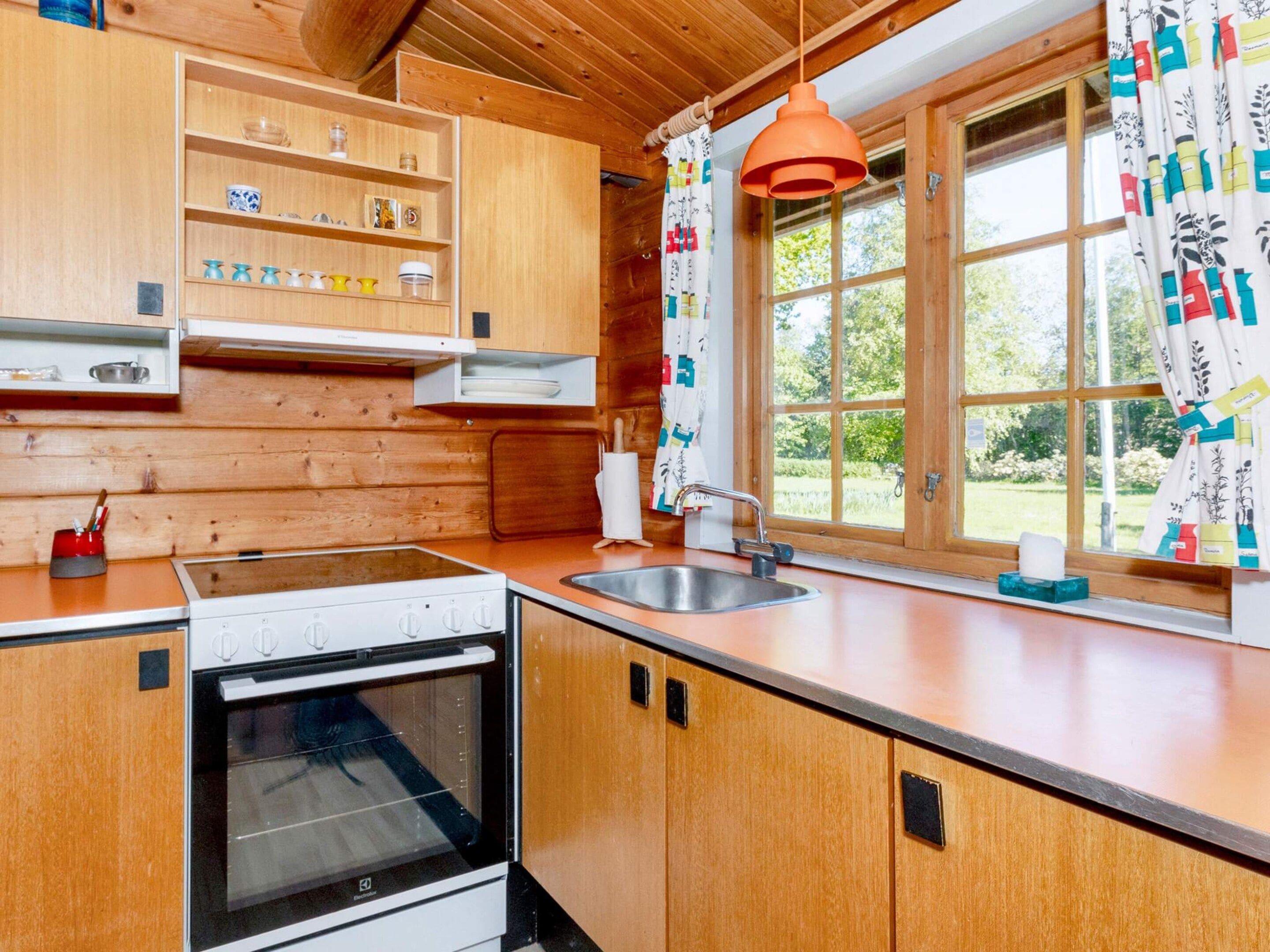 A kitchen with wooden cabinets, a stove, a sink, and a window with curtains.