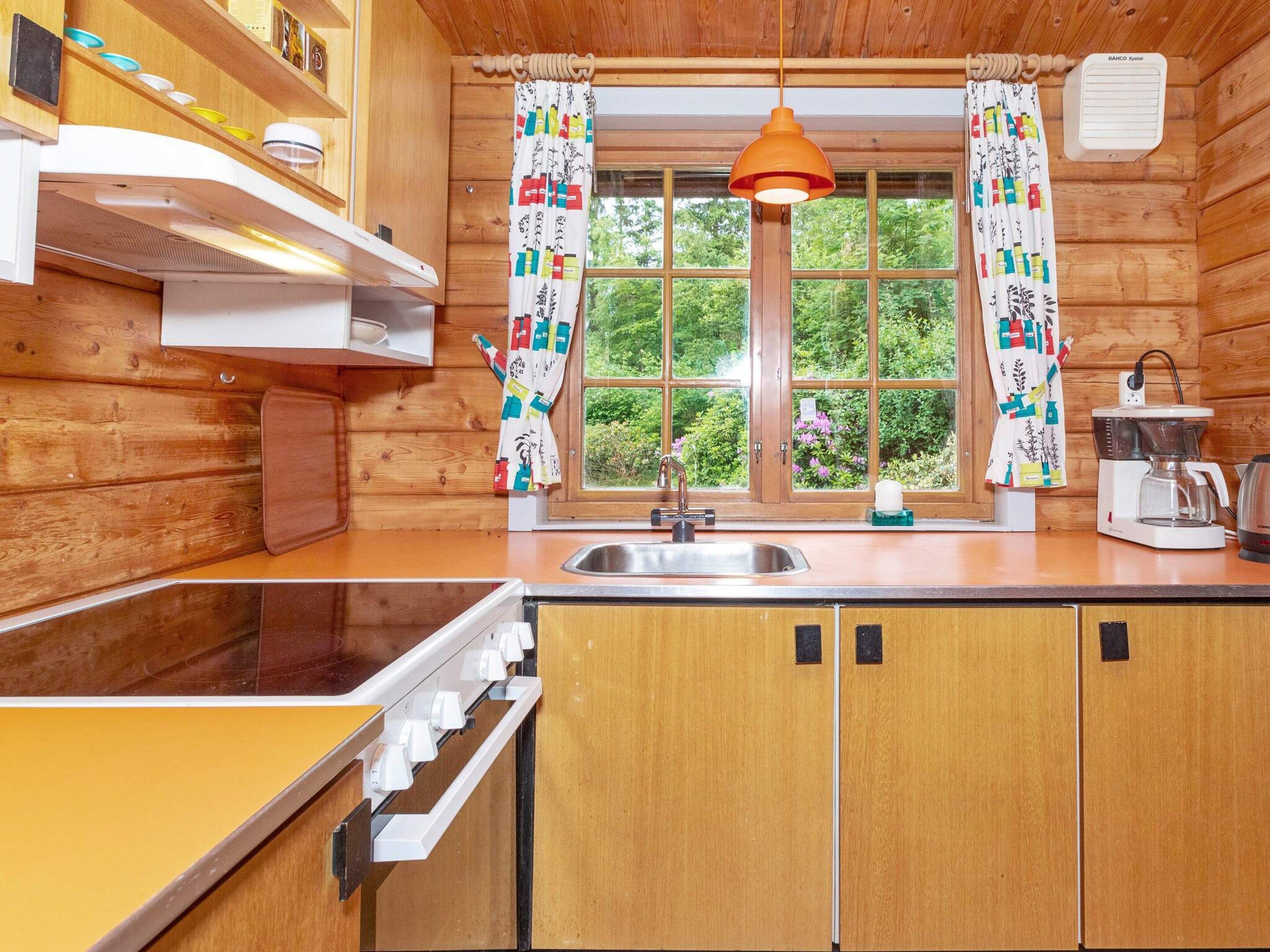 A wooden cabin kitchen with a window, a sink, a coffee maker, and a hanging pendant light.