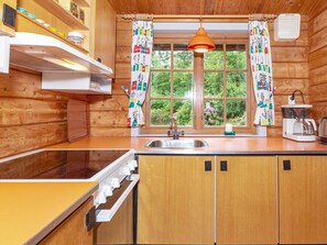 A wooden cabin kitchen with a window, a sink, a coffee maker, and a hanging pendant light. - 6 Person Holiday Home in Roslev (Roslev)