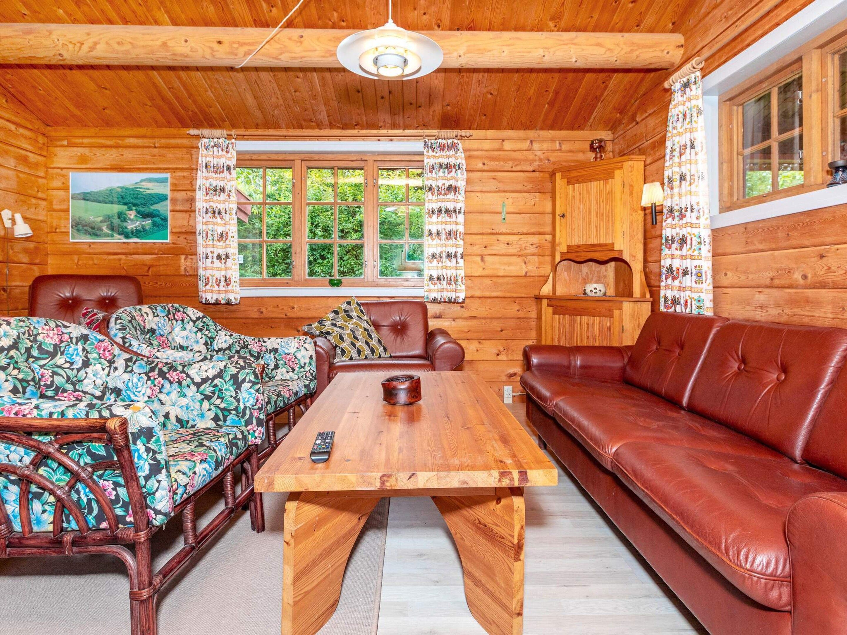 A cozy cabin interior with a wooden dining table, two sofas, and a window with curtains.