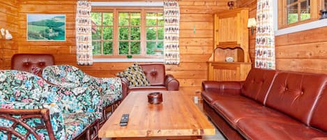 A cozy cabin interior with a wooden dining table, two sofas, and a window with curtains.